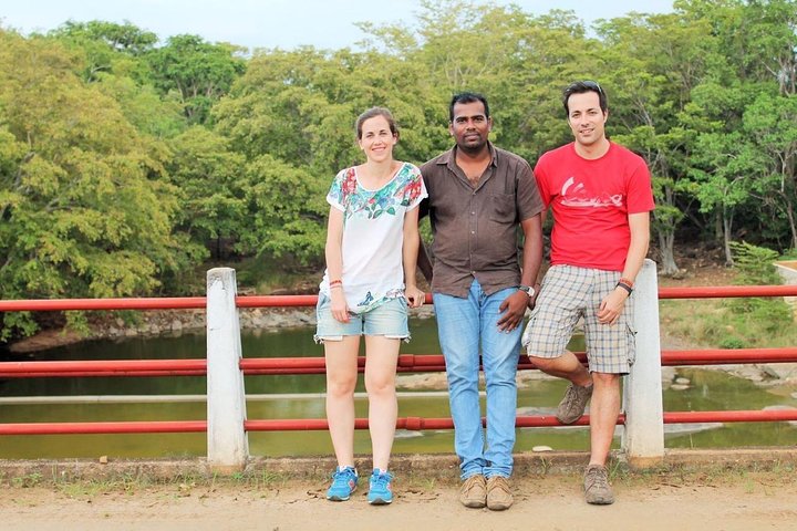 Two guests and their tour host beside a red railing with trees behind them