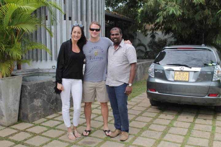 Two guests and their tour host beside a parked car
