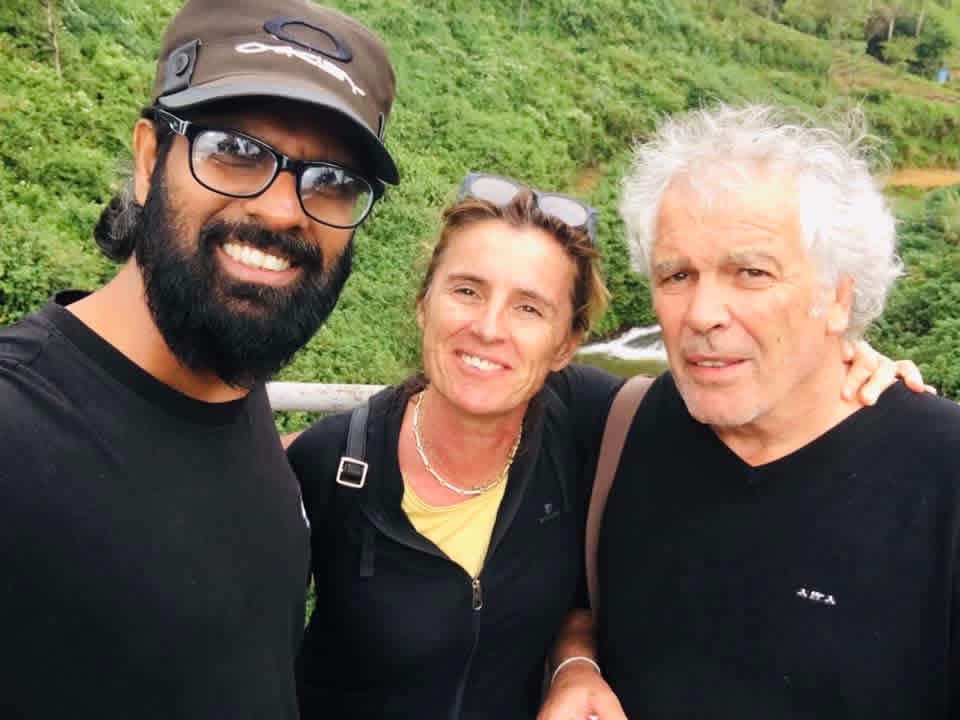 Two guests and their tour host smiling by a waterfall