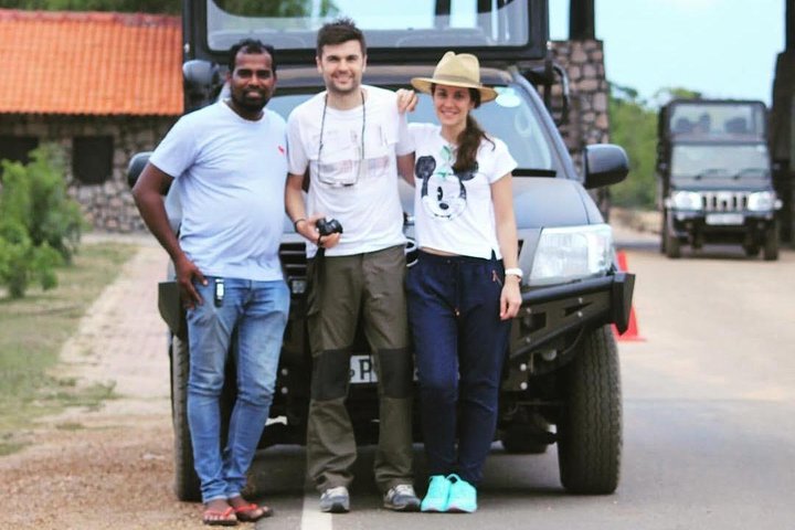 Two guests and their tour host beside a safari vehicle