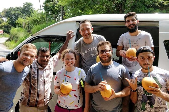 Travellers holding coconuts beside their tour vehicle