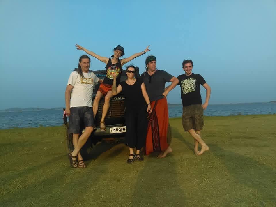 A group of travellers beside their safari jeep at sunset by the water